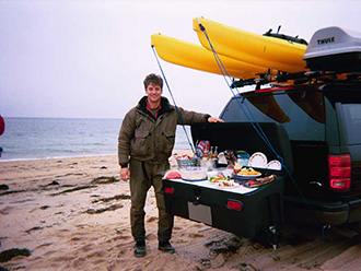Fisherman on beach standing next to picnic lunch served on StowAway Standard Cargo Carrier with Buffet Board accessories