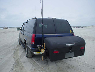 SUV driving on beach with StowAway Standard Cargo Carrier and Fishing Rod Holder attachment